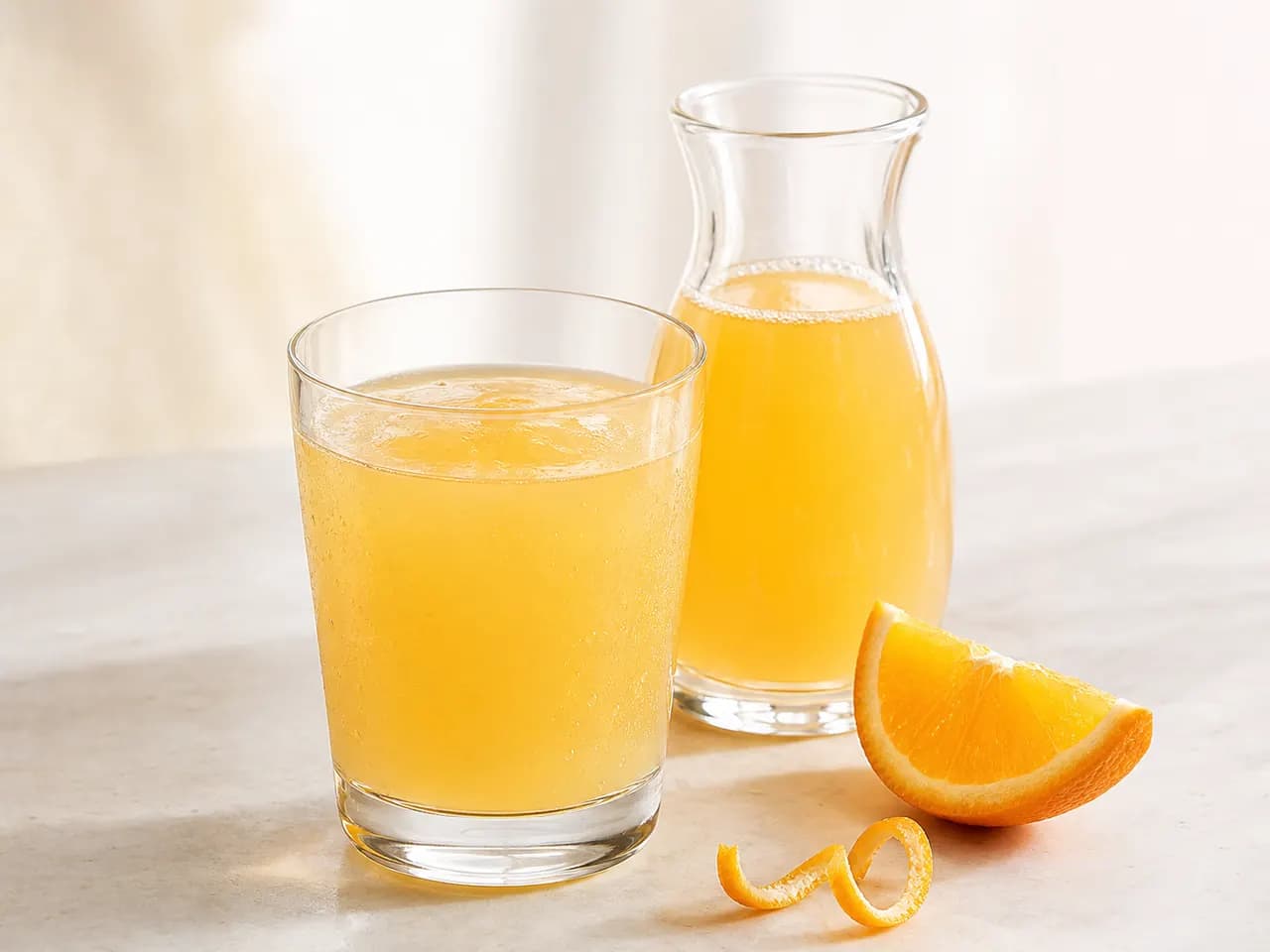 Finished golden-orange citrus beverage in a clear glass and carafe